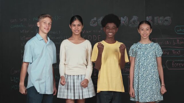Diverse academic student cheering and celebrate successful project while raised hand. Group of multicultural children standing at blackboard with engineering code while looking at camera. Edification