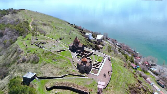 Aerial view of Sevanavank monastery complex on a green peninsula overlooking Lake Sevan with tourists walking along the paths in Sevan, Gegharkunik Province, Armenia.