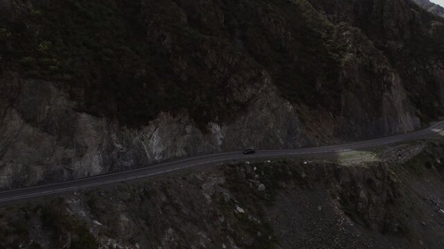 Drone footage of Chuysky Trakt mountain road carved into rocky cliffs beside the Katun River in Altai Republic, Russia, scenic travel route with cars and water