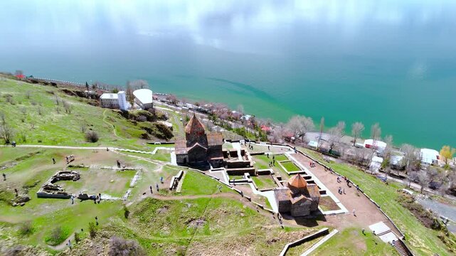 Aerial view of Sevanavank monastery complex with stone churches and ruins overlooking the lake with people walking along the paths in Sevan, Gegharkunik Province, Armenia.