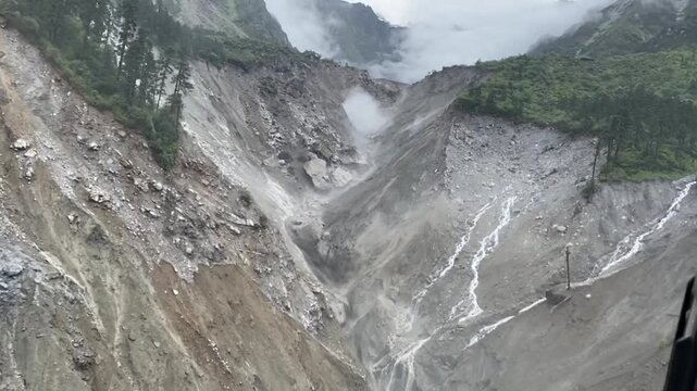 Aerial footage from helicopter capturing landslide activity in Nepal. Shows earth movement, damaged hillside, and rugged terrain in a mountain environment.