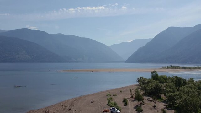 Drone footage of Teletskoye Lake with sandy spit, calm water and forested shore, surrounded by mountain ridges under a clear sky in Altai Republic, Russia