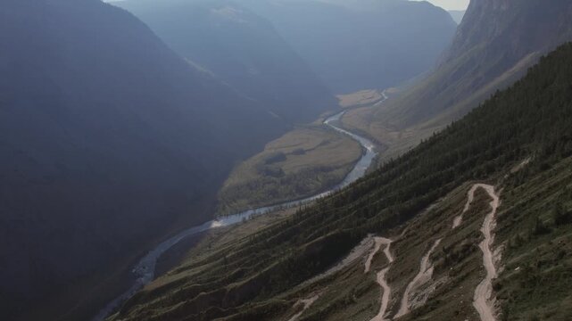 Aerial landscape of Katu-Yaryk Pass with steep dirt road switchbacks descending into the Chulyshman River valley, Altai Republic, Russia, in soft evening light