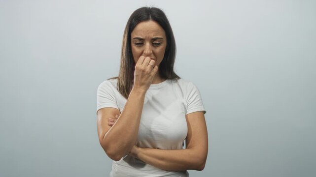 Woman biting fingernails with hand to mouth and crossed arm pose in studio setting; anxiety doubt hesitation.