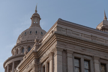 Fototapeta premium Close up angled view of the Texas State Capitol showing the east wing and central dome with statue on top against a clear blue sky.