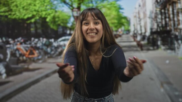 Young woman extends hands forward on a street, smiling with eyes closed as she reaches for a hug; joy connection.