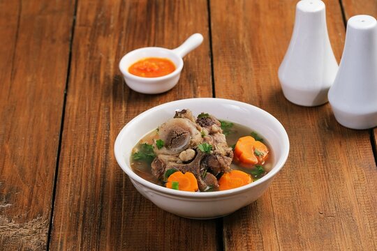 Sop Buntut Or Oxtail soup served with chili sauce and tableware, showcasing traditional Indonesian cuisine and dining concept.