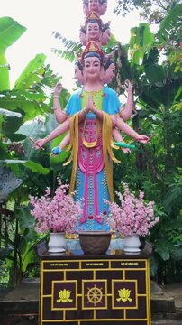 A statue of a multi-armed deity with peacocks and deer adorns a garden in Linh An Pagoda, Da Lat, Vietnam. The statue is a representation of Buddhist or Hindu mythology.