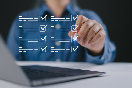 Hand using pen to check virtual checklist on laptop, representing task management, digital workflow, productivity, project planning, and online organization system.