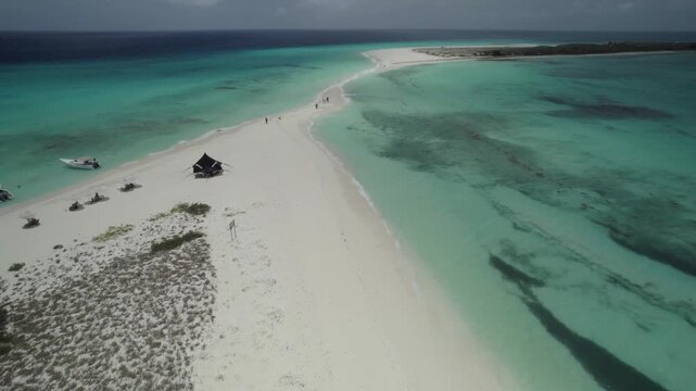 Drone tilt-up reveal Cayo de Agua in Los Roques National Park, Venezuela. Pristine white sandbar stretches between crystal-clear turquoise waters, forming a natural pathway across the Caribbean.