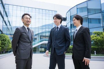 Fototapeta premium An image of businesspeople in suits conversing outdoors in front of a modern office building; the corporate sales team communicating with one another