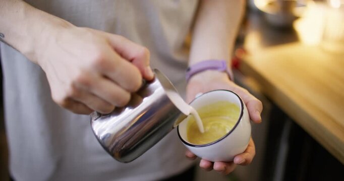 Latte art. Pouring foamed milk. Barista hand adding frothing steaming creamy liquid to aromatic beverage serving coffee in ceramic cup.