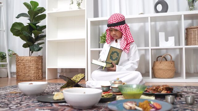 Arab muslim boy hands holding and reading the Holy Quran green book, Wearing traditional white thobe and red keffiyeh, Concept of Islamic religion, faith, Ramadan culture and education