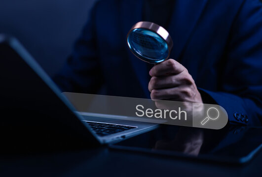 Cybersecurity expert using magnifying glass to search digital data on laptop computer, online investigation, internet search, data analysis and cyber protection technology concept.