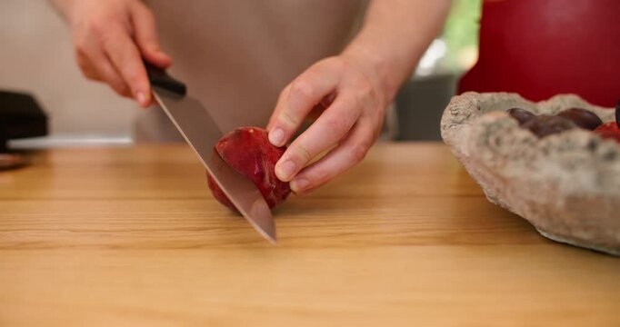 Ripe peach cutting. Fruit slicing. Unrecognizable experienced man chef hands using knife on wooden board cooking plums dessert at workplace.