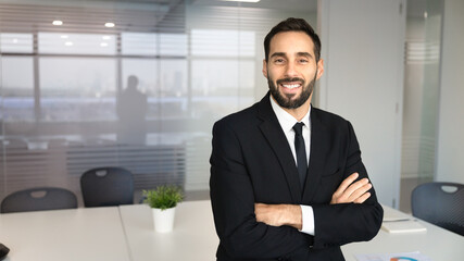 Fototapeta premium Smiling adult 30s Hispanic businessman, looking at camera, posing for professional business portrait standing in office meeting room, representing success, corporate employee and executive position