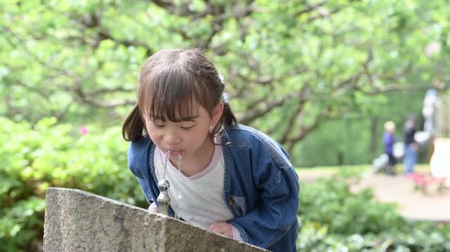公園の水飲み場で水分補給する女の子のポートレート新緑と遊ぶ、暑い日のイメージの動画