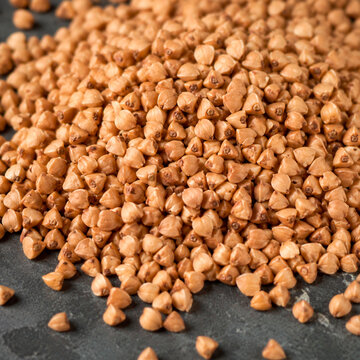 Extreme close-up of scattered toasted buckwheat groats revealing sharp pyramidal shapes and rich brown hues resting on a dark slate surface with shallow depth of field