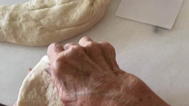 A close-up captures hands skillfully stretching and expanding the edges of a dough wrapper to prepare it for filling during the handmade baozi making process.