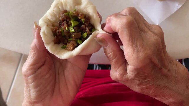 A close-up shot captures hands skillfully pleating the dough to complete a traditional handmade baozi filled with a savory mixture of minced meat and petai.