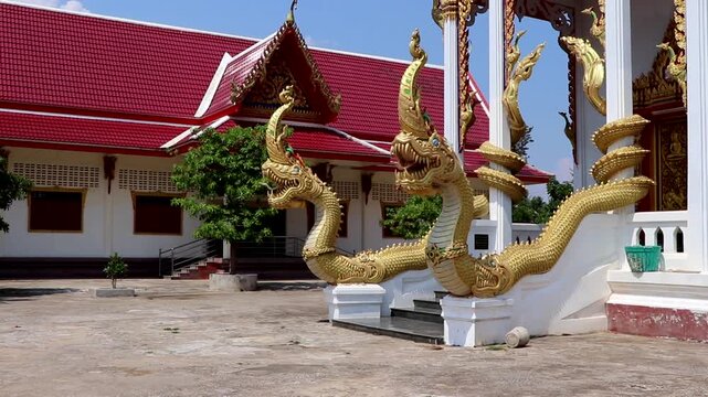 Ornate golden naga serpent statues guard the entrance of a traditional Buddhist temple in Da Nang, Vietnam. The red-roofed temple and intricate architecture reflect the rich culture.