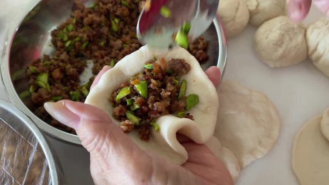 A close-up captures hands using a spoon to place a mixture of minced meat and stink beans (petai) onto a circular dough wrapper to prepare traditional handmade baozi.