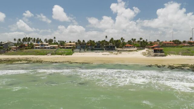 Taiba beach in Sao Goncalo do Amarante municipality Ceara state Brazil South America with beachfront resort houses and palm trees along sandy shoreline with waves drone forward flyover aerial shot
