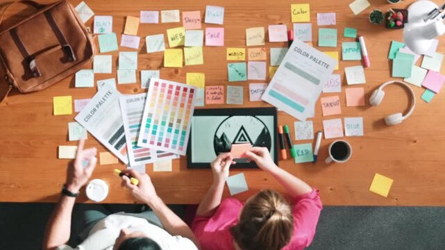 Top view of smart designer holding color palette while project manager looking at design and choosing color for program. Professional businesswoman taking a note while design creative logo. Symposium.