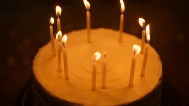 Birthday cake with lit candles glowing against dark background