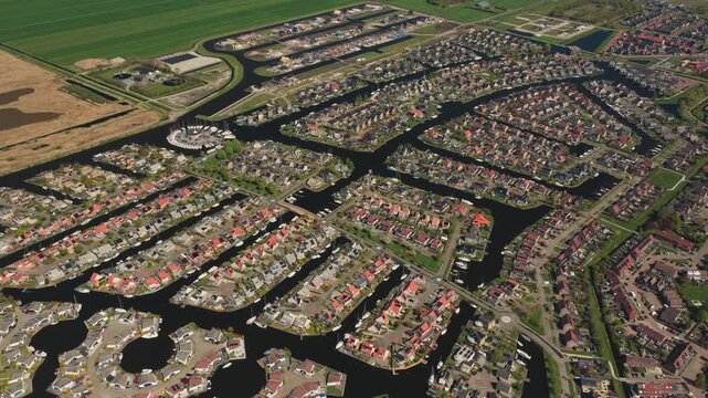 Aerial view of modern residential houses built along a network of canals and waterways surrounded by green fields in Lemmer, Friesland, Netherlands.