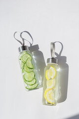Obraz premium Top view of infused water in glass bottles with lemon and cucumber, modern minimal layout. Takeaway home made healthy detox drink with natural ingredients for sport, fitness, everyday self care.