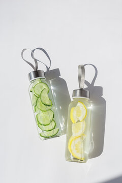 Top view of infused water in glass bottles with lemon and cucumber, modern minimal layout. Takeaway home made healthy detox drink with natural ingredients for sport, fitness, everyday self care.