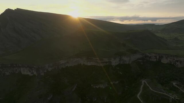 Aerial footage of a winding mountain road and deep green valley at sunset near Keger village, Republic of Dagestan, Russia, with sun rays over rugged ridges