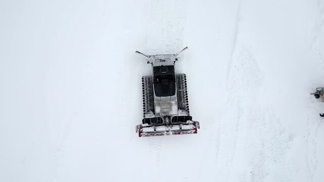 Snow groomer machine on a ski slope, top down view.