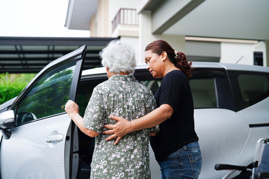 Caregiver help Asian elderly woman disability patient get in her car.