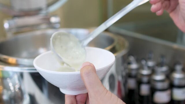 Ladling Hot Breakfast Porridge into a White Bowl at a Buffet Station