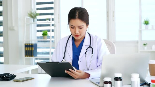 Doctor reading patients file.Asian doctor examining patient information form , working in office.