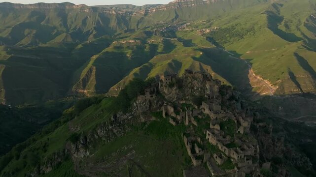 Drone footage of Gamzutl abandoned aul on a rocky ridge, surrounded by green Caucasus mountains at golden hour, Dagestan, Russia, scenic travel landscape
