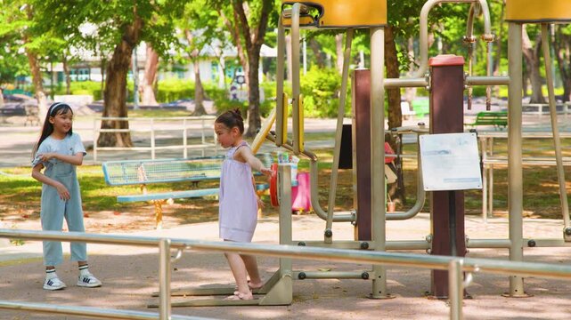 Two Young Asian Girls Playing on Outdoor Exercise Equipment in Park