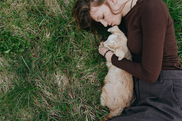 Naklejka premium Carefree woman on grass gently cuddling a young goat kid, capturing a tranquil countryside moment. Natural light highlights affection, nature, and simple rural living.