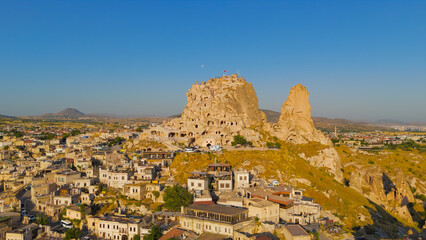 Uchisar, Nevsehir, Turkey. Dominant Uchisar Castle rock formation towering above Cappadocia landscape with surrounding village at sunrise.. Aerial View © Video Render