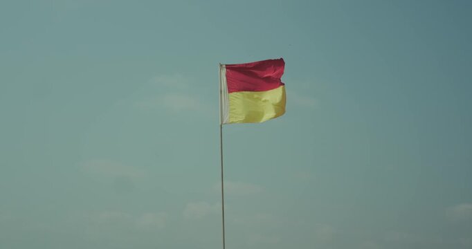 Red and yellow lifeguard warning flag on pole against clear sky beach safety concept
