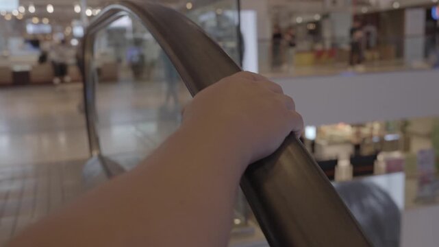 pov close up to hand holding handheld of escalator while going up on escalator in department store, movement of the man's hand on the escalator handrails