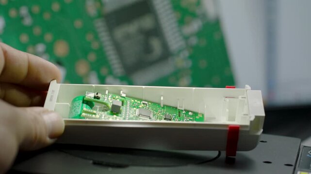 Hand holds small electronic circuit board inside white plastic housing, circuit background