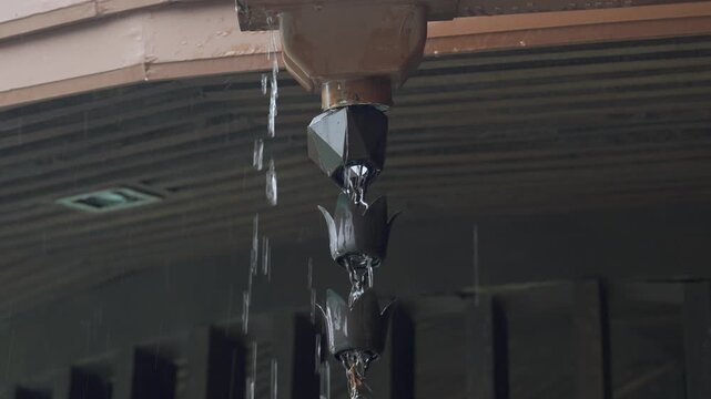 A copper rain chain with water flowing down from a roof gutter,Close-up of a traditional Japanese kusari-doi during a rainstorm. Natural calm rain fall background