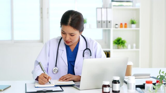 Doctor looking at laptop screen writing in notebook for research planning or medical tech innovation in hospital office. Healthcare medic worker, research.