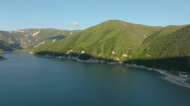 Drone footage of Kezenoyam Lake surrounded by green mountain slopes and rocky shores in the Caucasus Mountains, Chechnya Republic, Russia, on a clear day