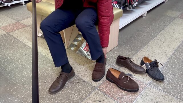A male customer sits in a shoe boutique surrounded by various styles of classic men's footwear while testing the fit and appearance of new shoes.