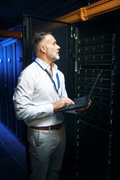 Mature, man or server room with laptop for network security, maintenance or repair service. Male person, IT technician or engineer with computer or mainframe machine for storage backup in data center