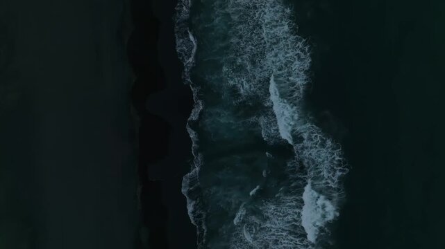 Top-down aerial footage of ocean waves rolling onto black volcanic sand at Khalaktyrsky Beach, Kamchatka Krai, Russia, dramatic seascape texture
